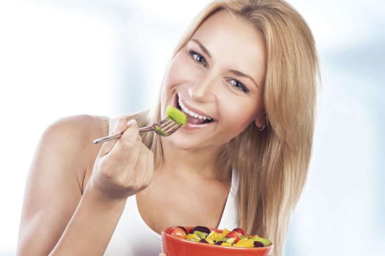 Portrait of pretty blond woman eating fresh tasty fruit salad on the kitchen at home, special fruity diet, enjoying organic nutrition and healthy lifestyle