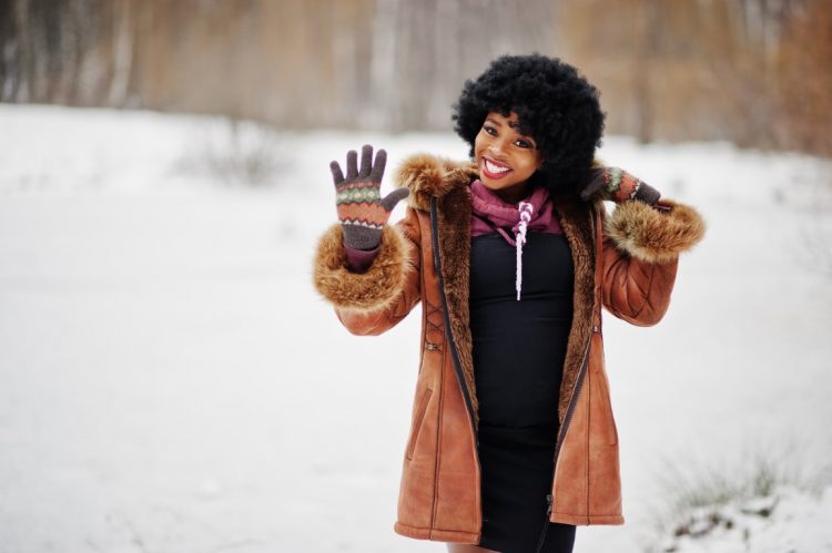 Curly hair african american woman wear on sheepskin coat and gloves posed at winter day, show five fingers.